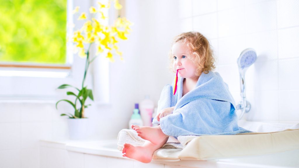 Little Girl With a Toothbrush in Her Mouth Wrapped in a Cozy Towel